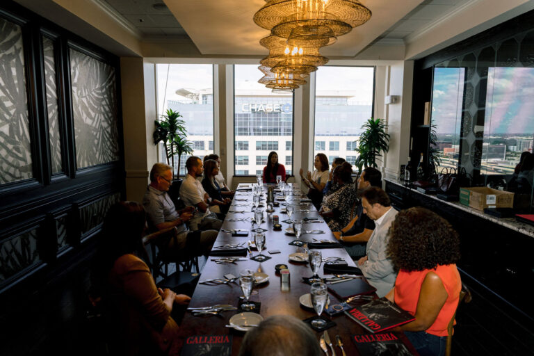 The Curator Circle seated along a long table under chandeliers at the Citrus Club, windows onto downtown Orlando behind them.