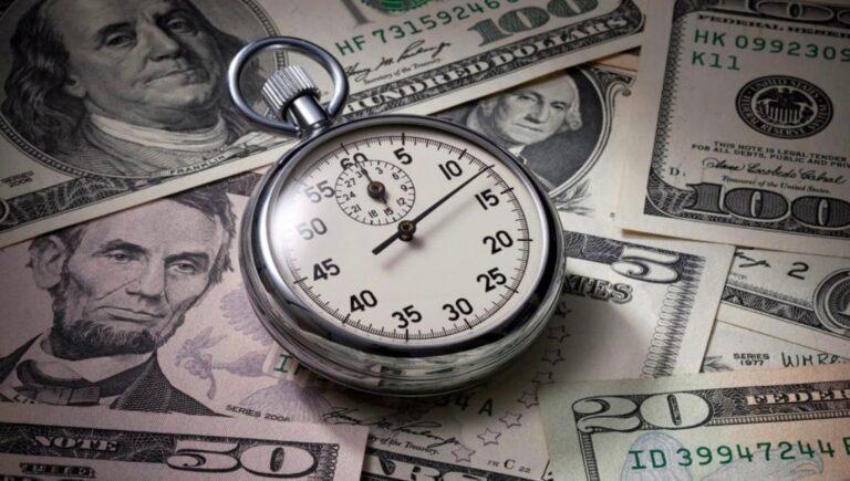 A silver stopwatch resting on a spread of United States banknotes