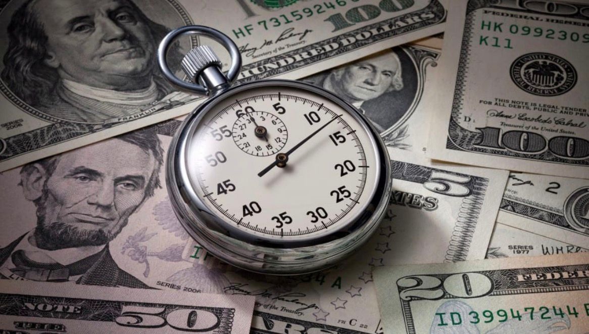 A silver stopwatch resting on a spread of United States banknotes