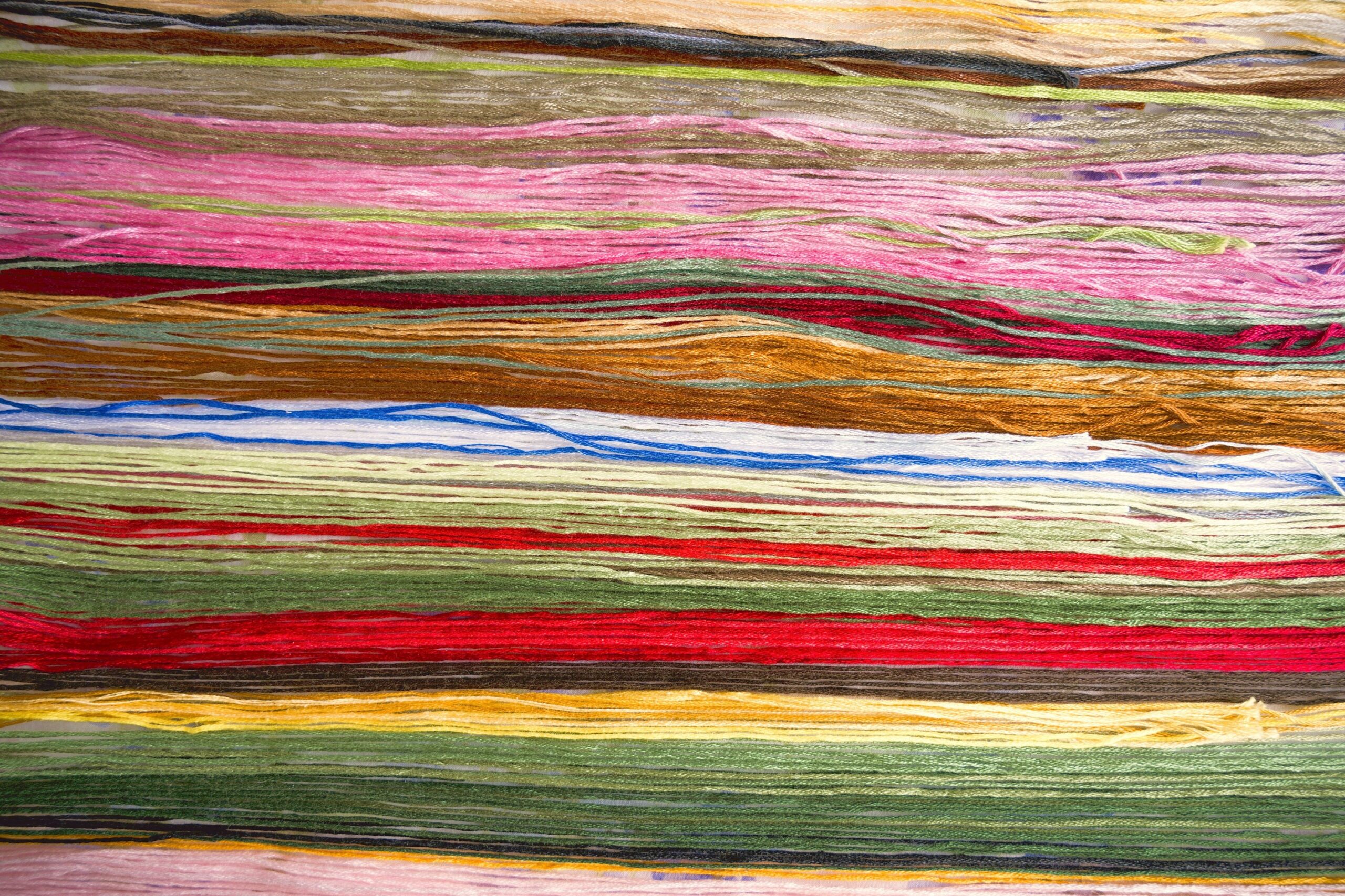 Bundles of dyed yarn laid in horizontal bands of pink, ochre, blue, green, red and yellow.