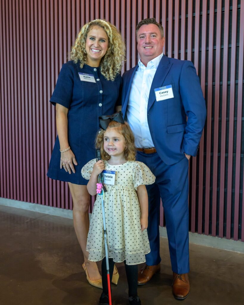 A young girl holding a white cane stands with two adults at a Lighthouse Central Florida event