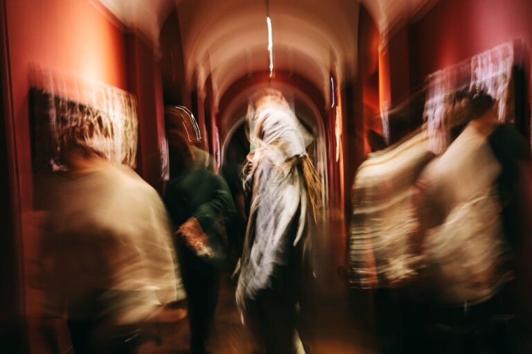 Visitors blurred in motion through a vaulted, red-walled gallery corridor, caught in a long exposure.