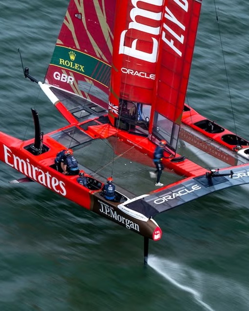 Great Britain's red F50 seen from above, flying on its foils with the crew in helmets on deck